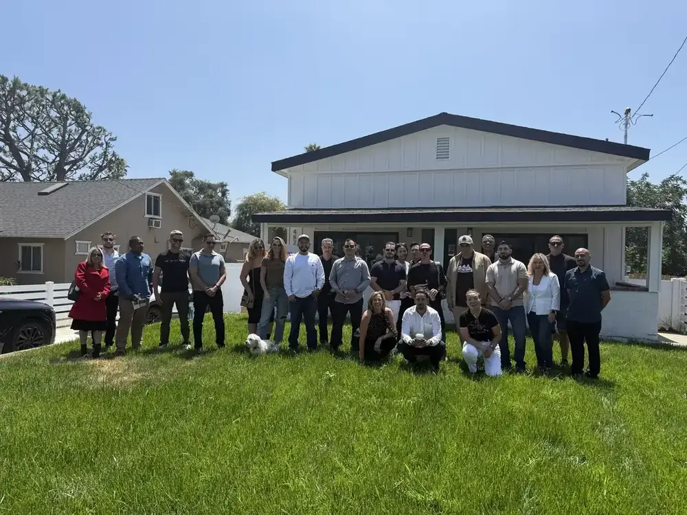 The Drive Thru Offers team and community gathered in front of a renovated home